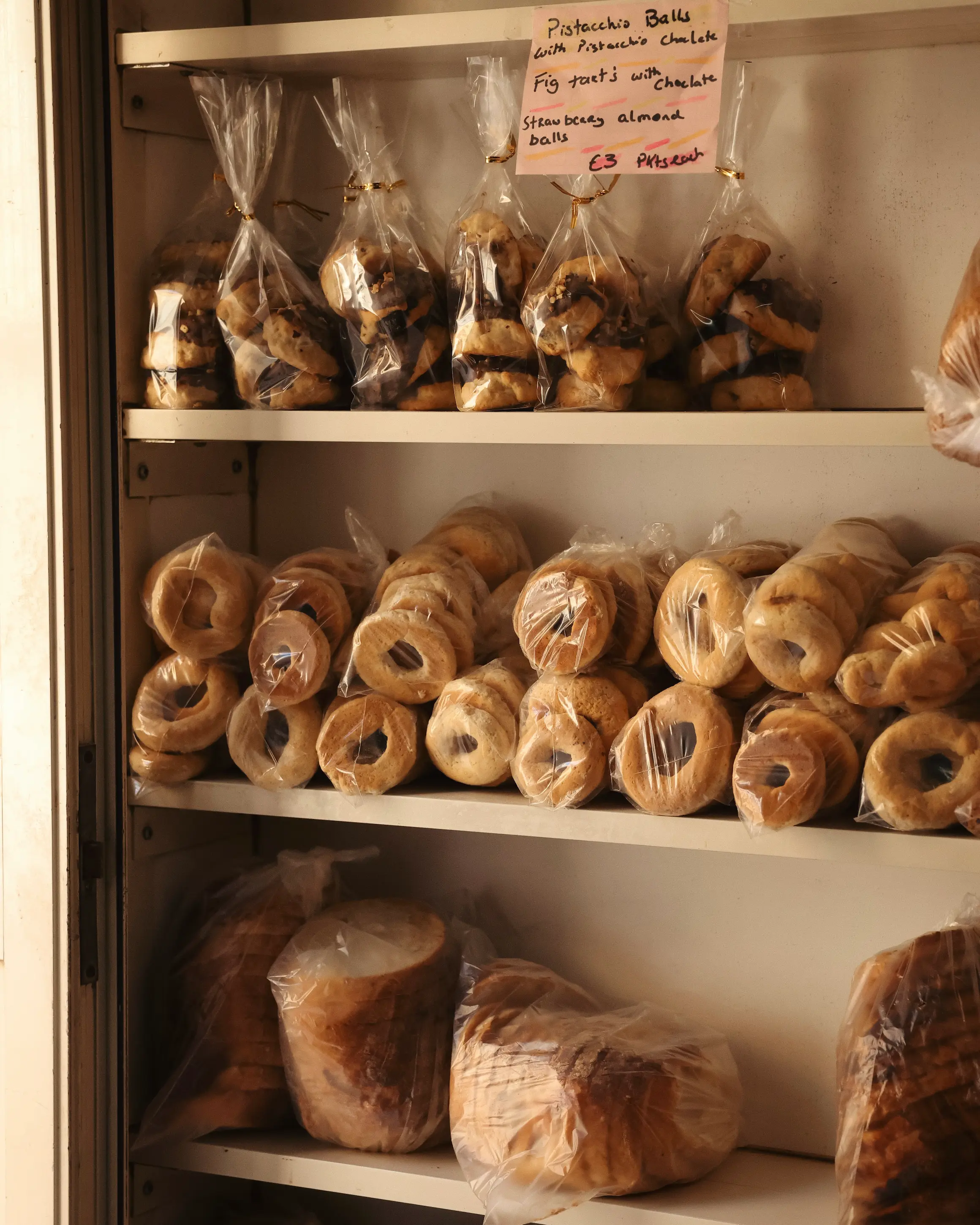 Fresh Maltese bread, ring-shaped pastries and sweet baked treats displayed on shelves inside Carmelo Micallef Bakery in Malta.