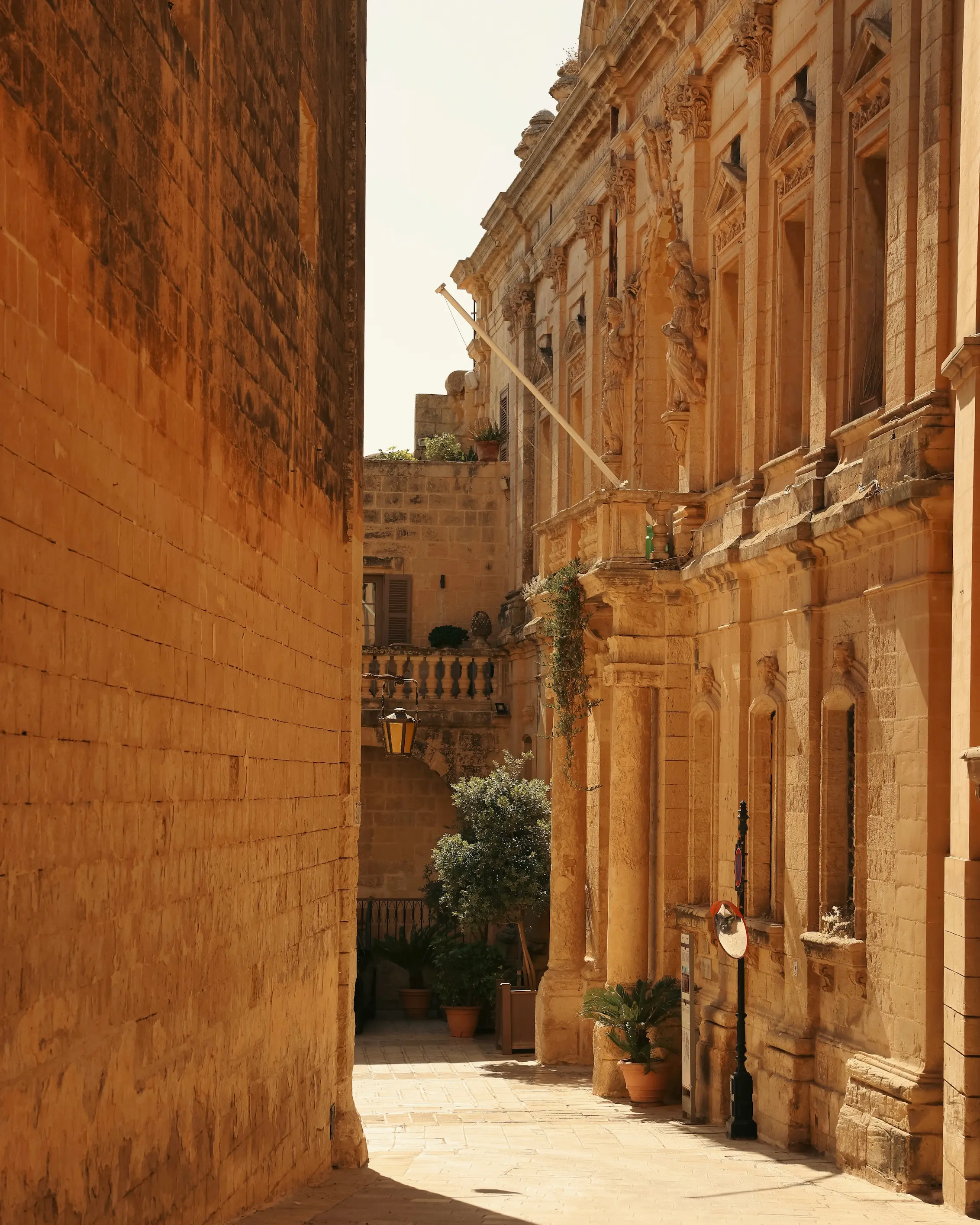 Historic limestone buildings lining a narrow sunlit street in Rabat, Malta, with ornate architecture and warm golden stone facades.