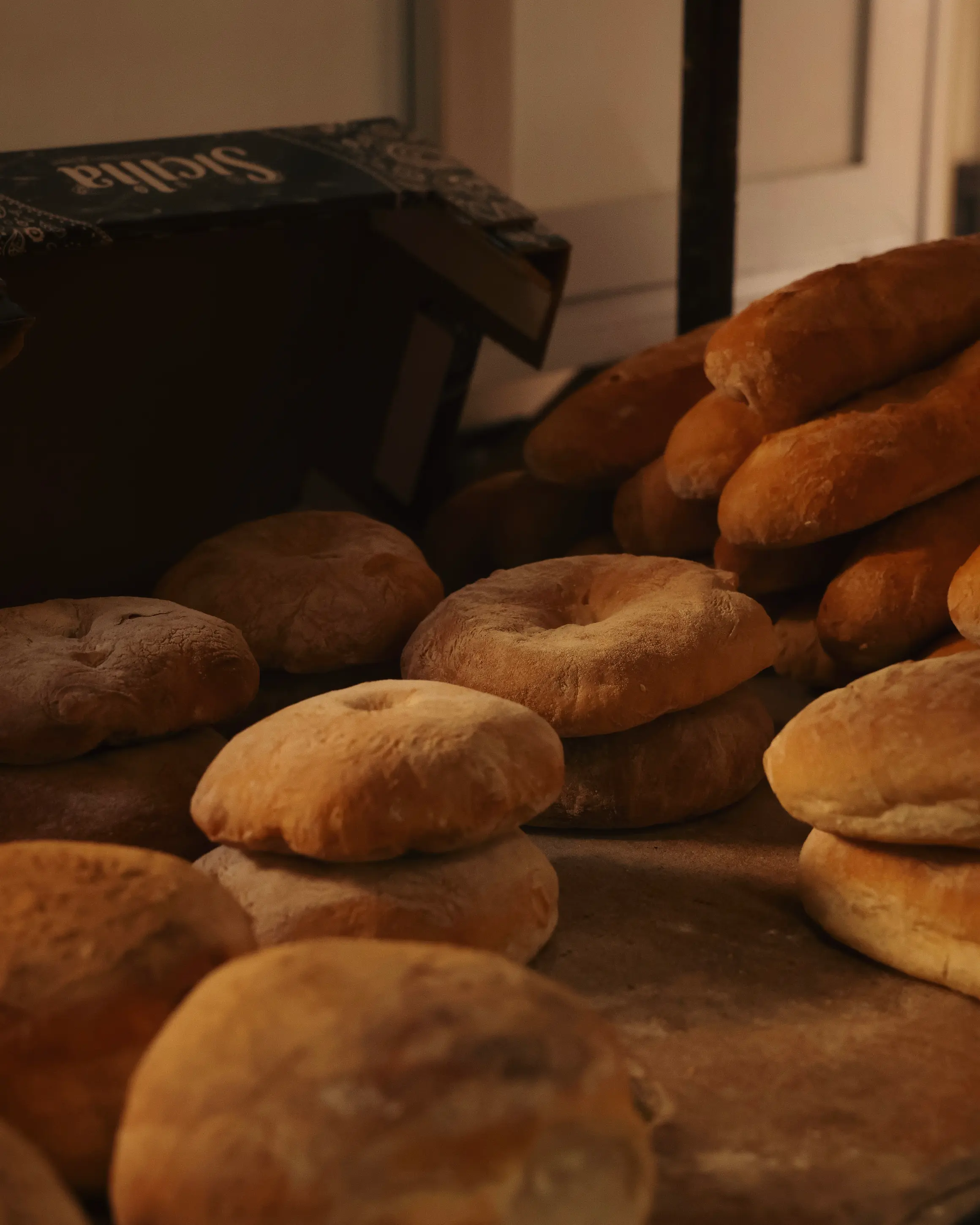 Freshly baked Maltese ftira bread stacked inside a traditional bakery, illuminated by warm morning light.