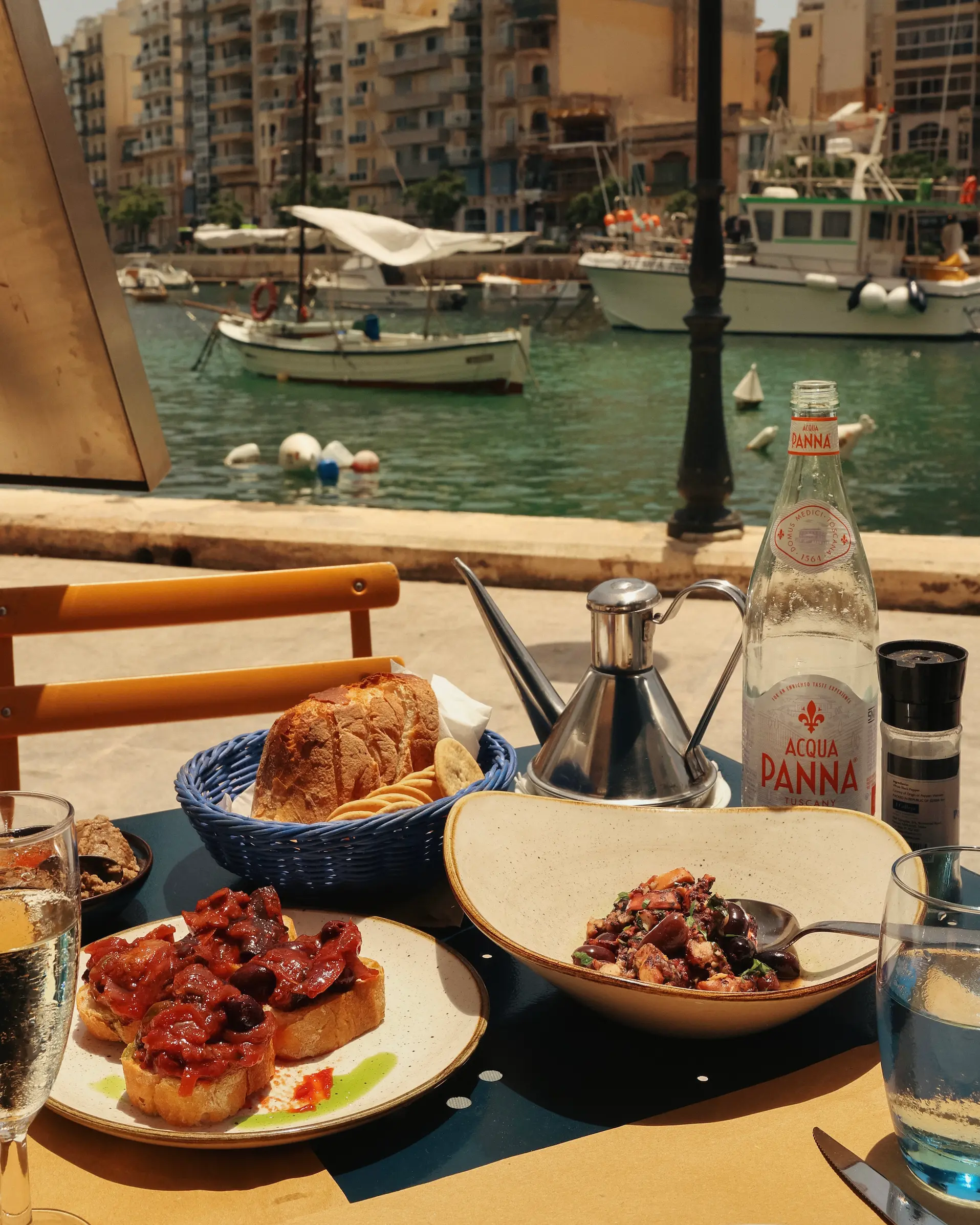 Traditional Maltese dishes served on a waterfront table at Gululu restaurant, overlooking fishing boats and the harbour in Malta.
