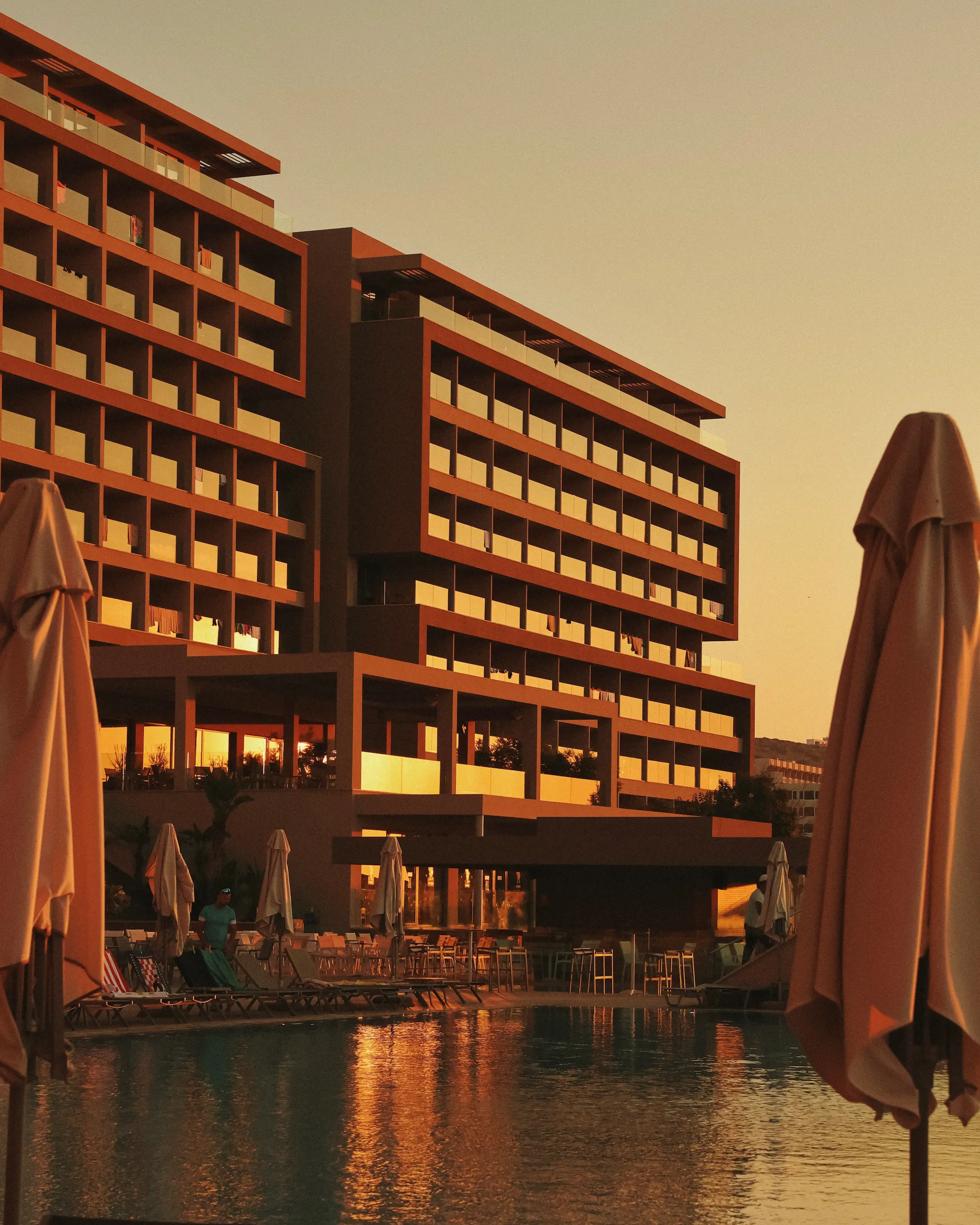 Golden hour over the swimming pool at Amada Colossos Resort in Rhodes, Greece, with the hotel glowing in the evening sun.