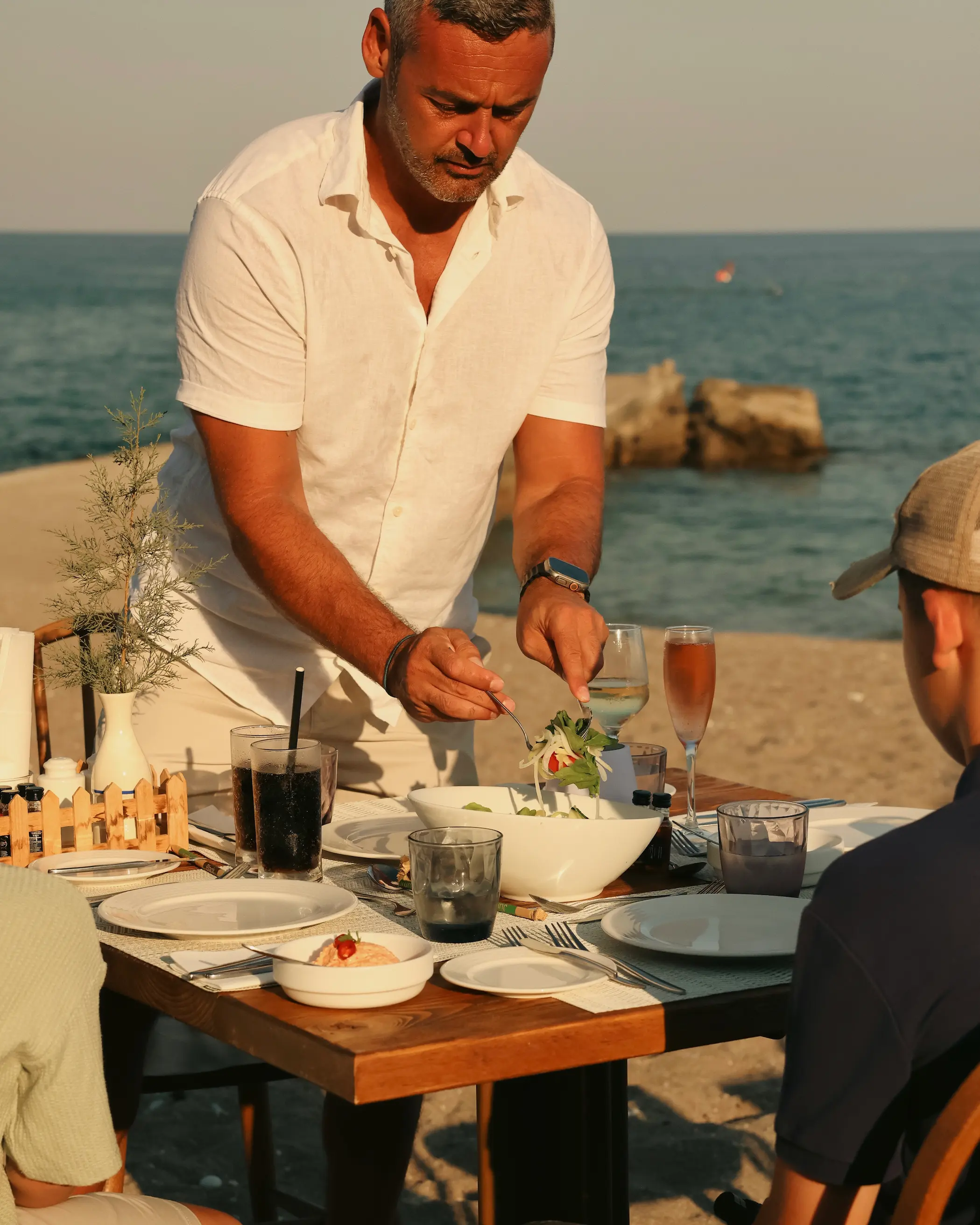 Family dining at Enalia Seaside Restaurant at Amada Colossos Resort in Rhodes, with dinner being served beside the beach at golden hour.