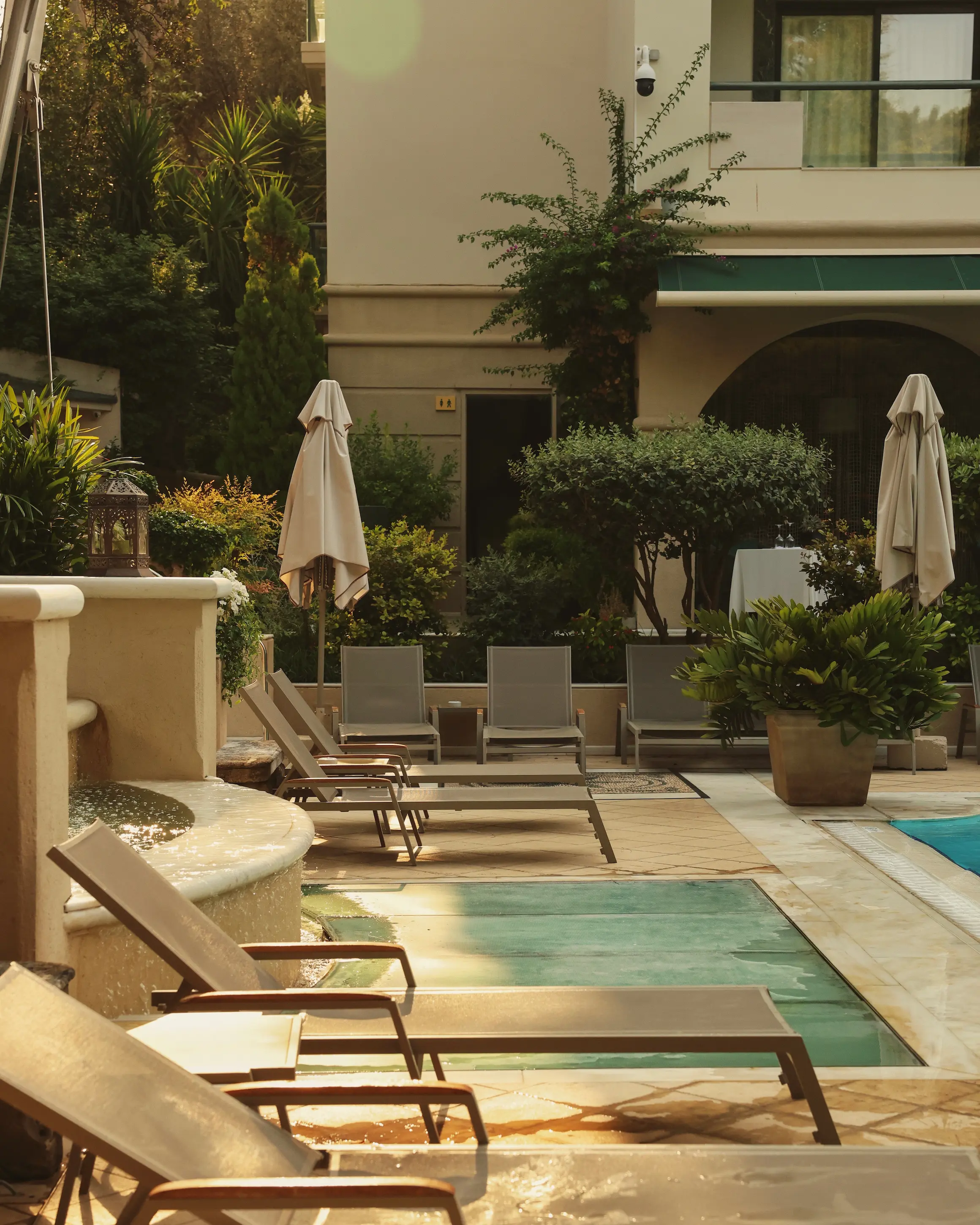 Poolside area at Rodos Park in Rhodes, with sun loungers, greenery and the boutique hotel surrounding the pool.