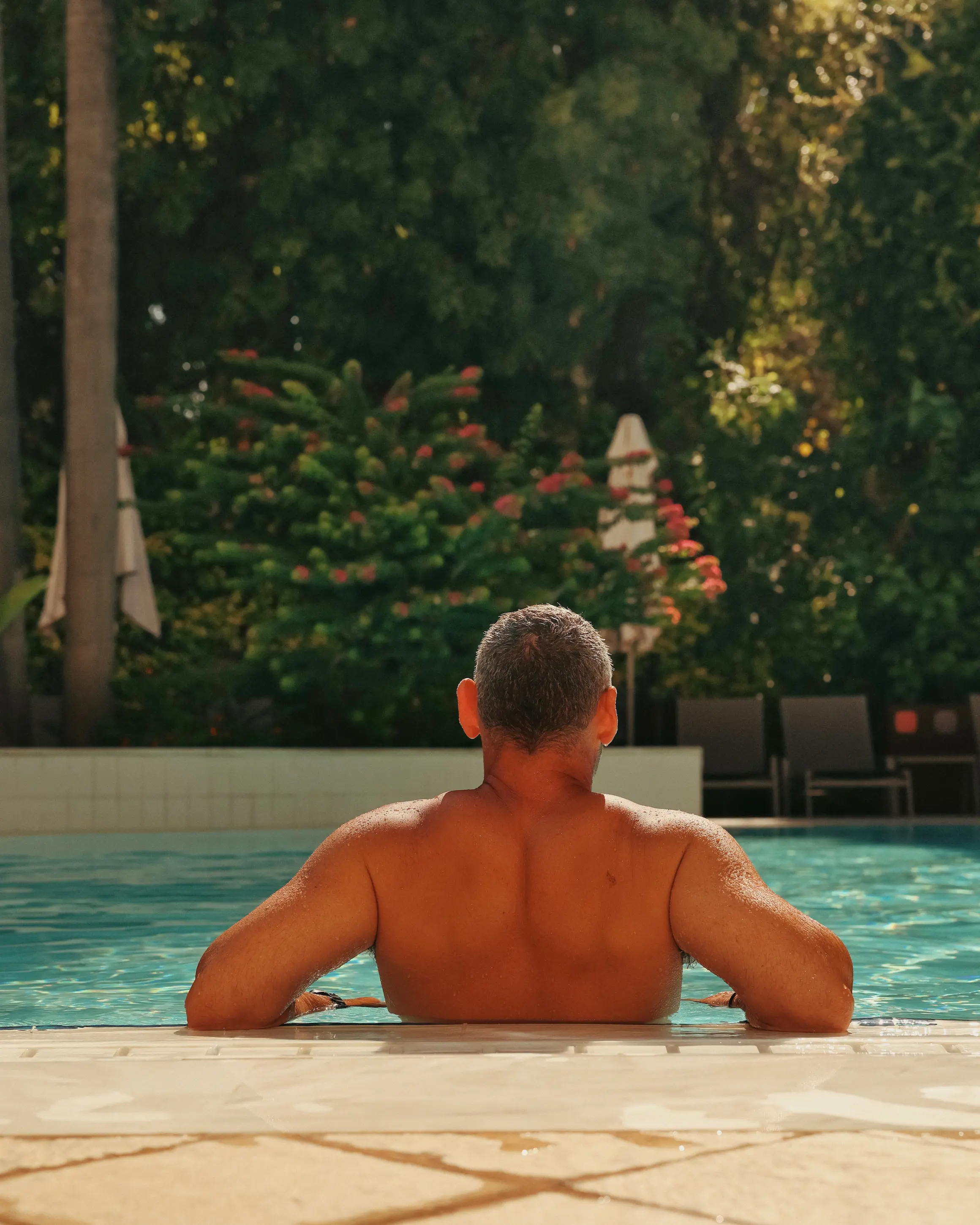 Guest relaxing in the swimming pool at Rodos Park in Rhodes, surrounded by lush greenery and shaded loungers.