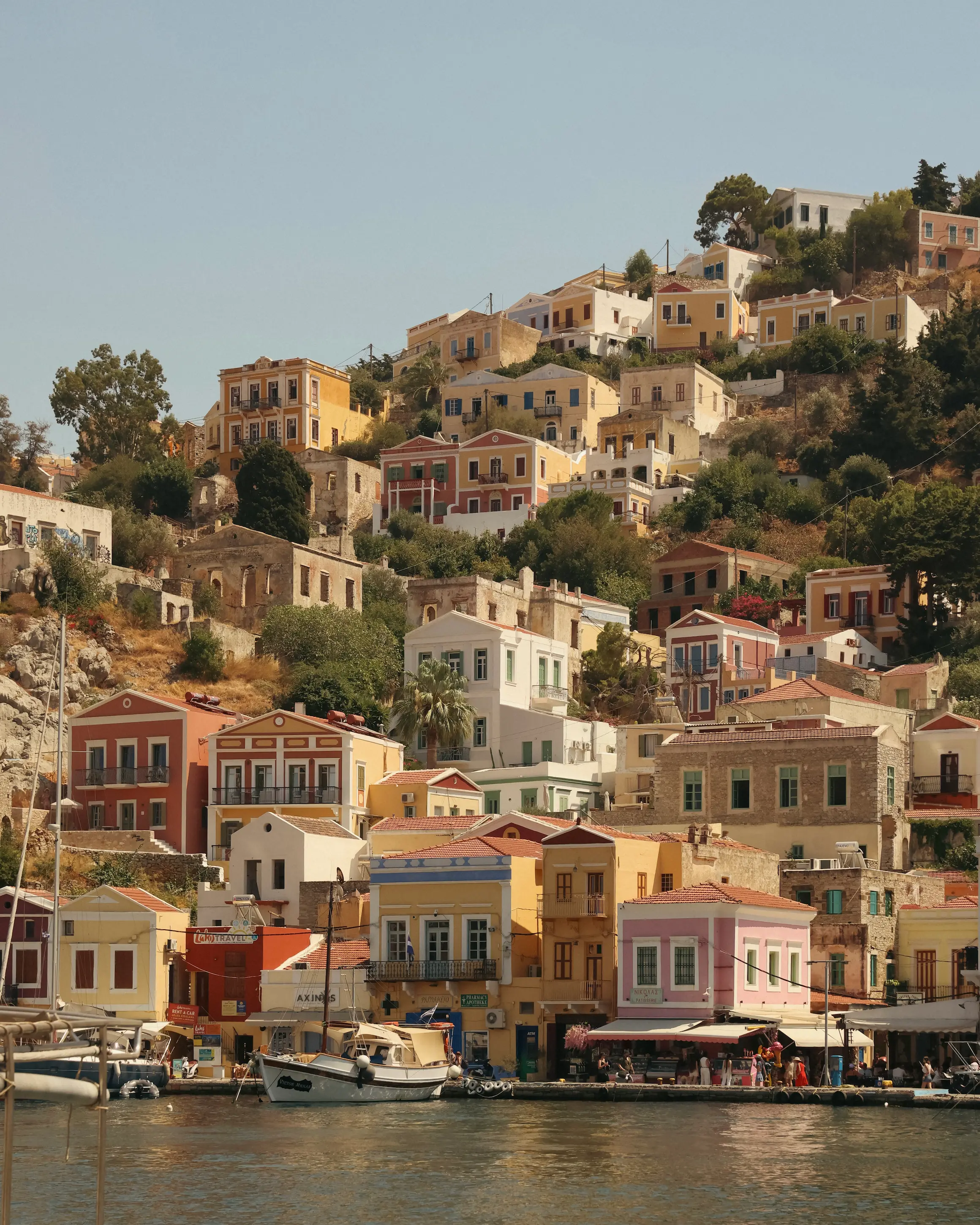 Colourful neoclassical houses climbing the hillside above the harbour on Symi island, Greece.
