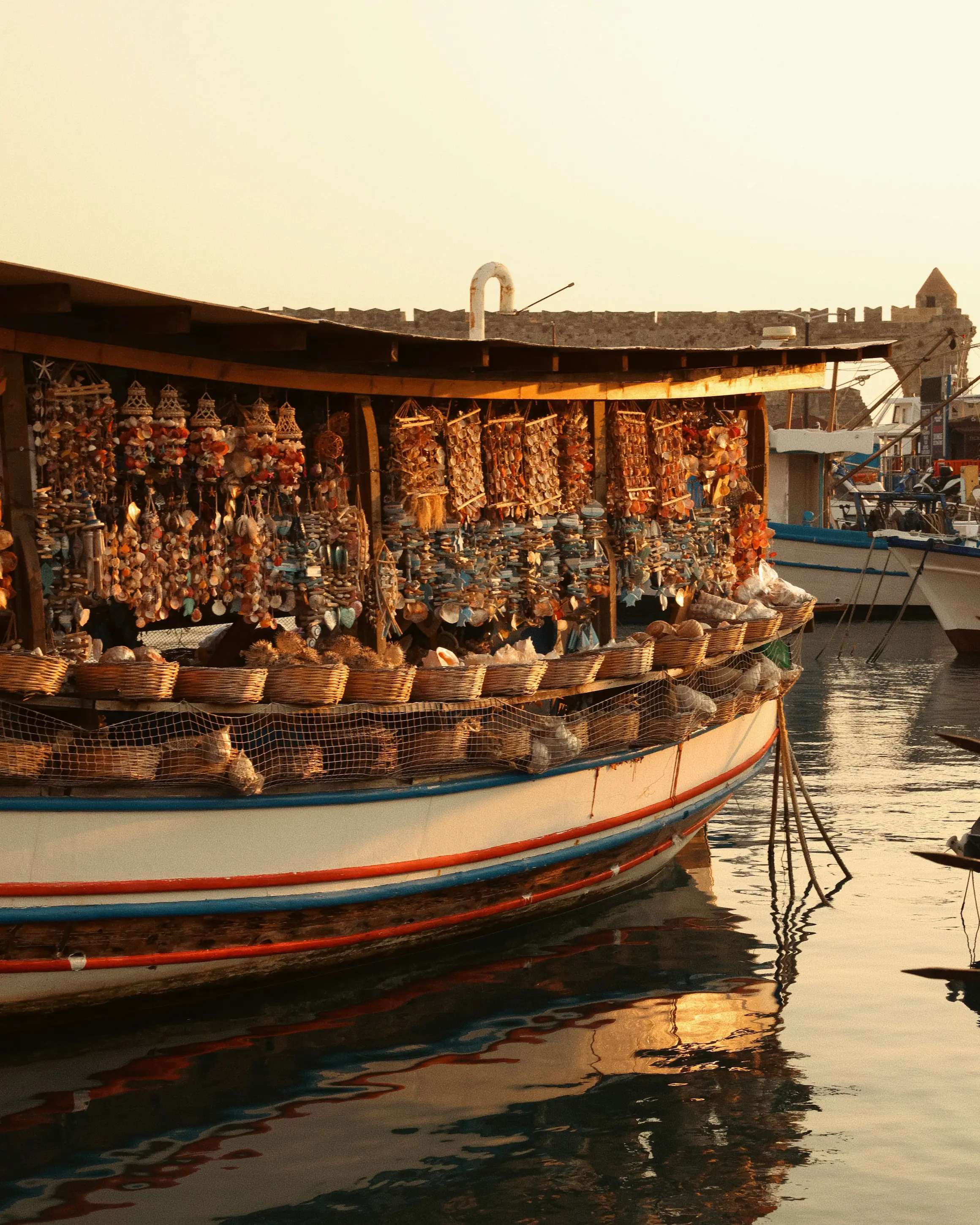 Traditional souvenir boat covered with shells and handmade decorations in Mandraki Harbour, Rhodes, at golden hour.