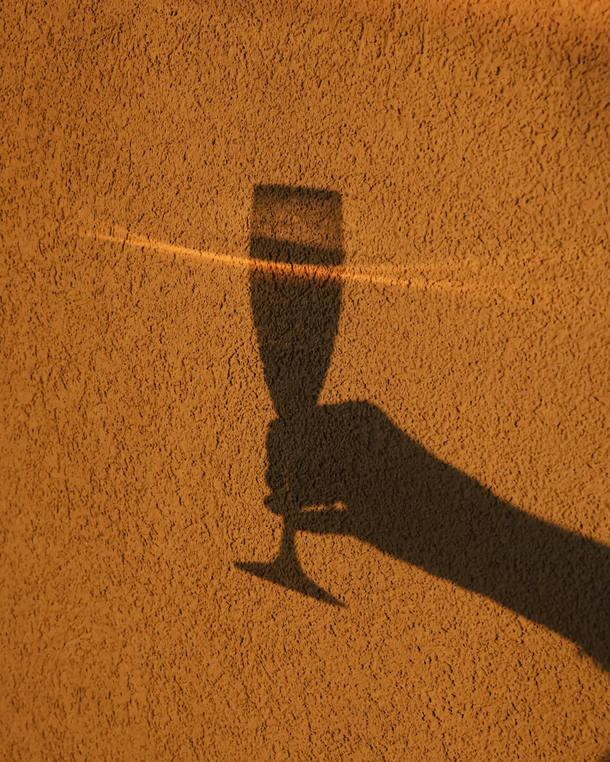 Shadow of a hand holding a cocktail glass cast onto a warm textured wall at golden hour in Rhodes.