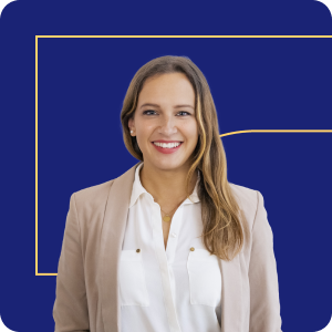 Smiling woman with long light brown hair wearing a beige blazer over a white blouse, standing against a navy blue background with a subtle yellow geometric line.