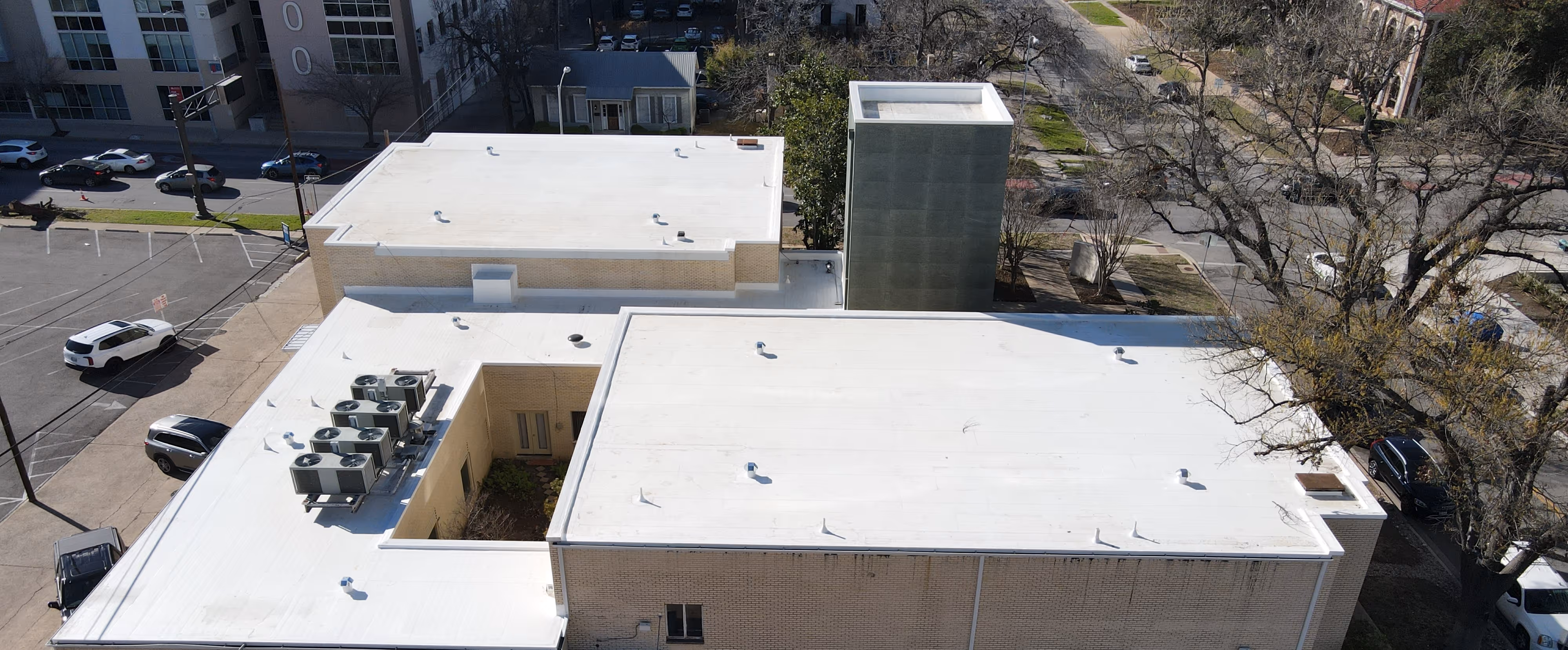 Aerial view of a building with a white commercial roof and rooftop equipment.