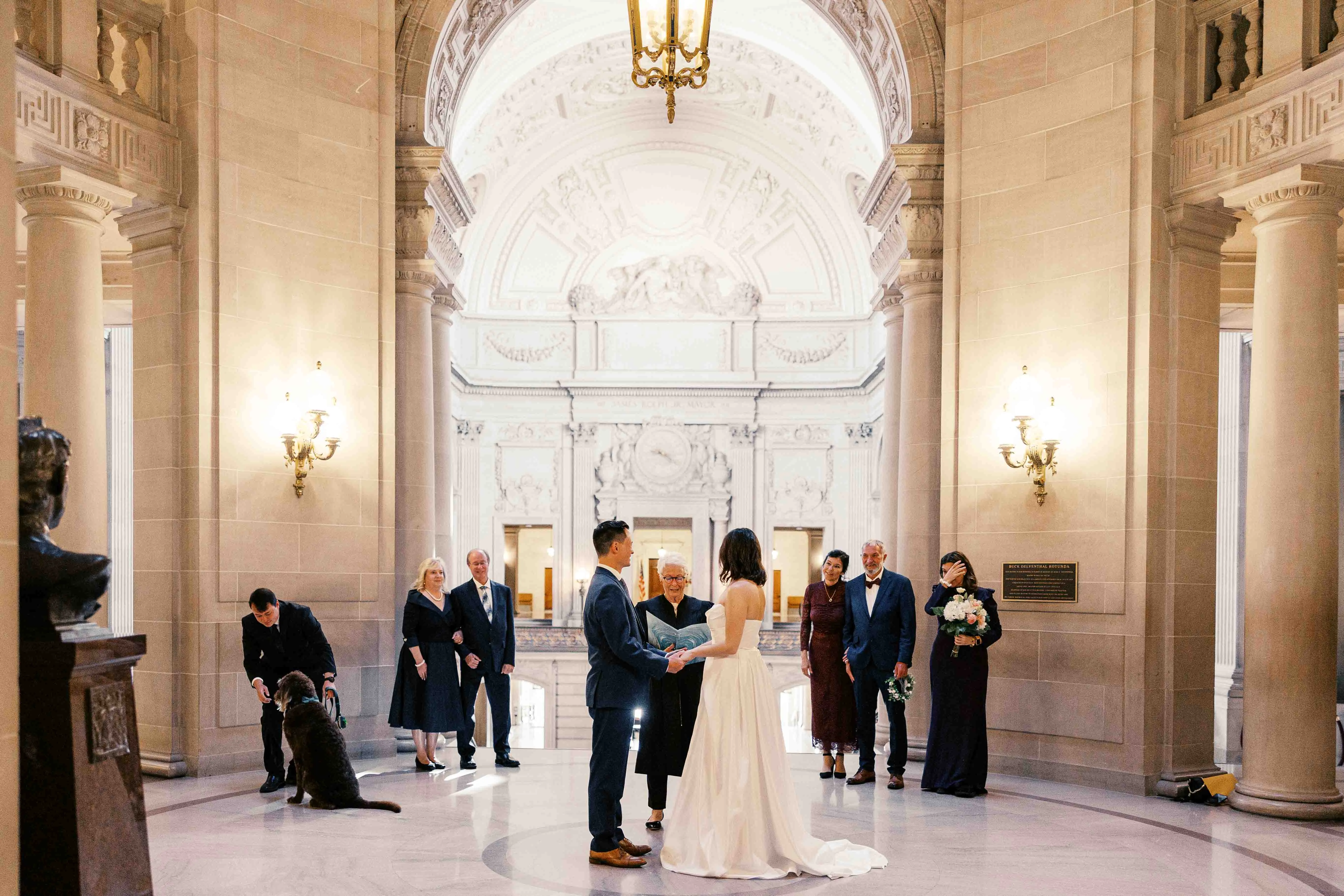 Bride and groom during their civil ceremony while eloping at San Francisoc City Hall, their family is around them crying and smiling, including their dog; documentary photography at san francisco city hall 