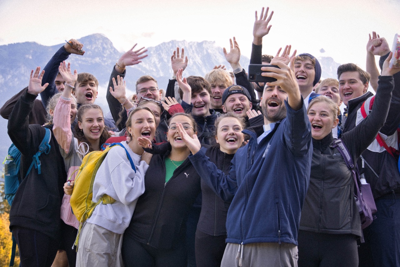GrowDeep Jugendliche machen gemeinsam mit Pater Andrew ein Gruppenfoto in den Bergen und jubeln und lachen.