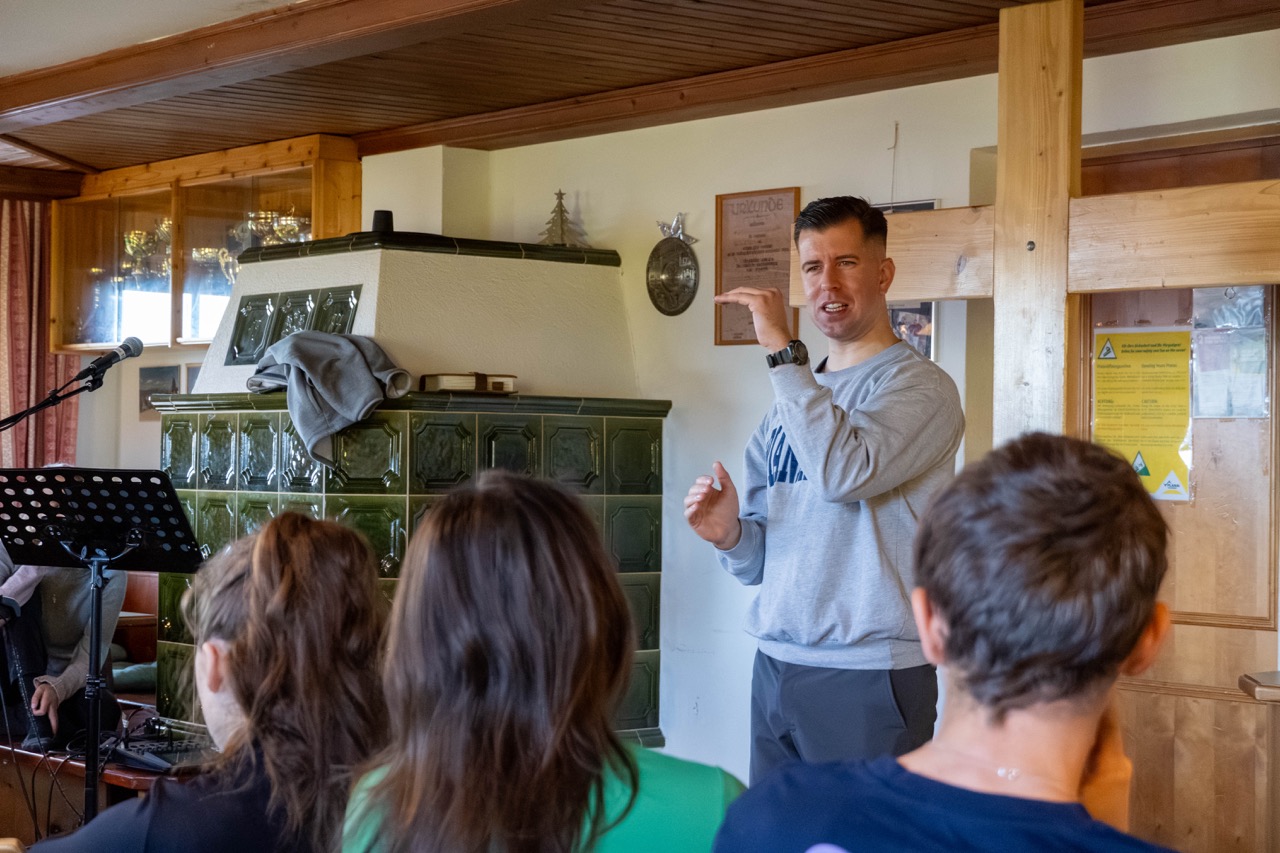 Lukas Bösche hält beim GrowDeep Wochenende einen Vortrag vor jungen Erwachsenen mit einem holzkreuz im Hintergrund