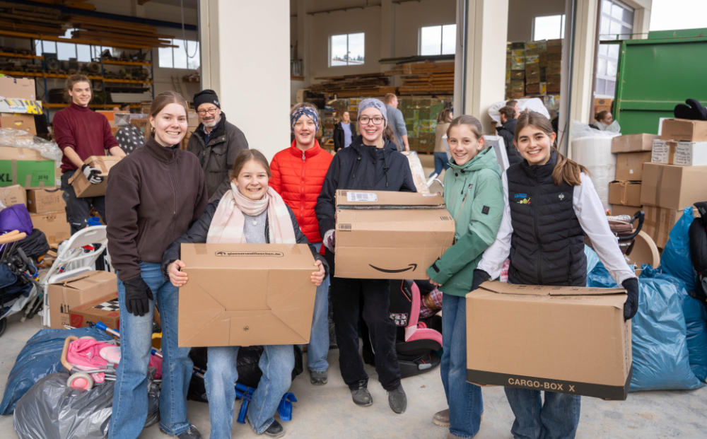 Gruppe junger Erwachsener trägt große Kartons mit Sachspenden in einer Lagerhalle bei Aktion Junge Leute helfen