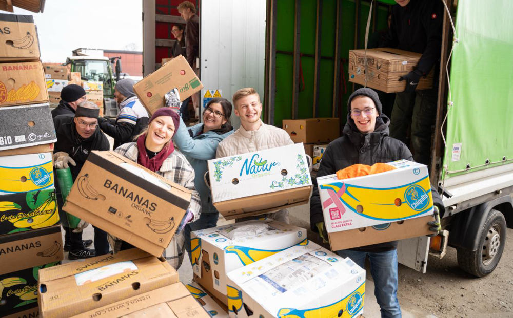 Junge Leute helfen: Gruppe junger Erwachsener lädt lachend Bananenkisten von einem Lkw bei Sammelaktion in Großbergham