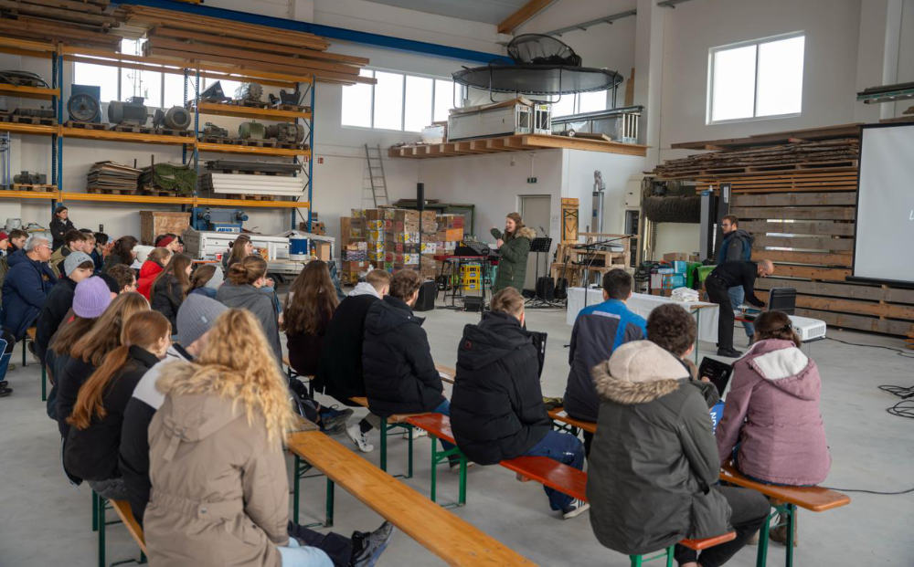 Grow Deep Wochenende: junge Erwachsene sitzen in einer Halle und hören einen Vortrag vor Paletten und Hilfsgütern in Südostbayern