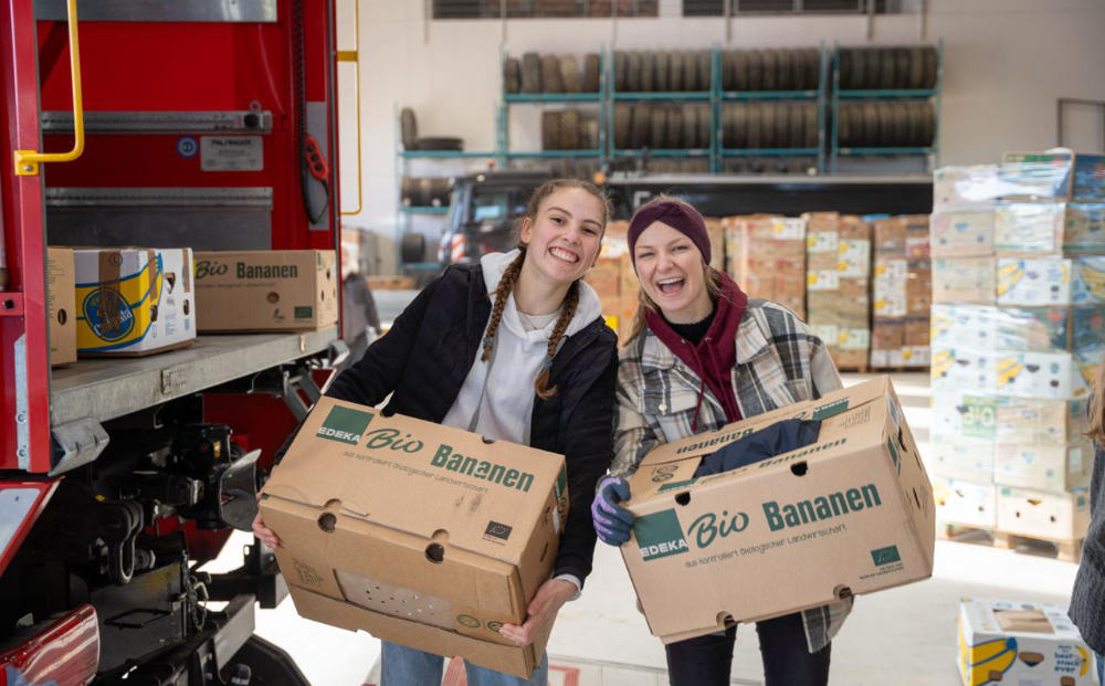 Zwei junge Frauen tragen Kartons mit Spenden vor einem Lkw bei Hilfsprojekt Junge Leute helfen in Südostbayern