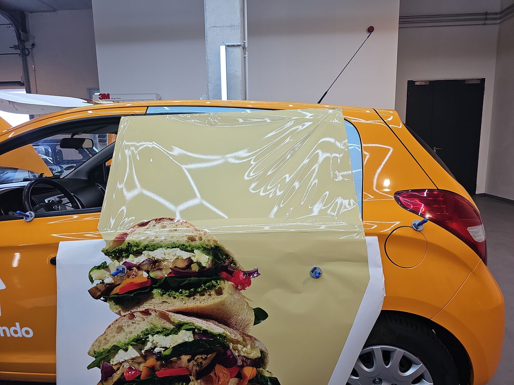 Verarbeitung der Wrapping-Folie am Fahrzeugheck, im Hintergrund das 3M-Folienlager