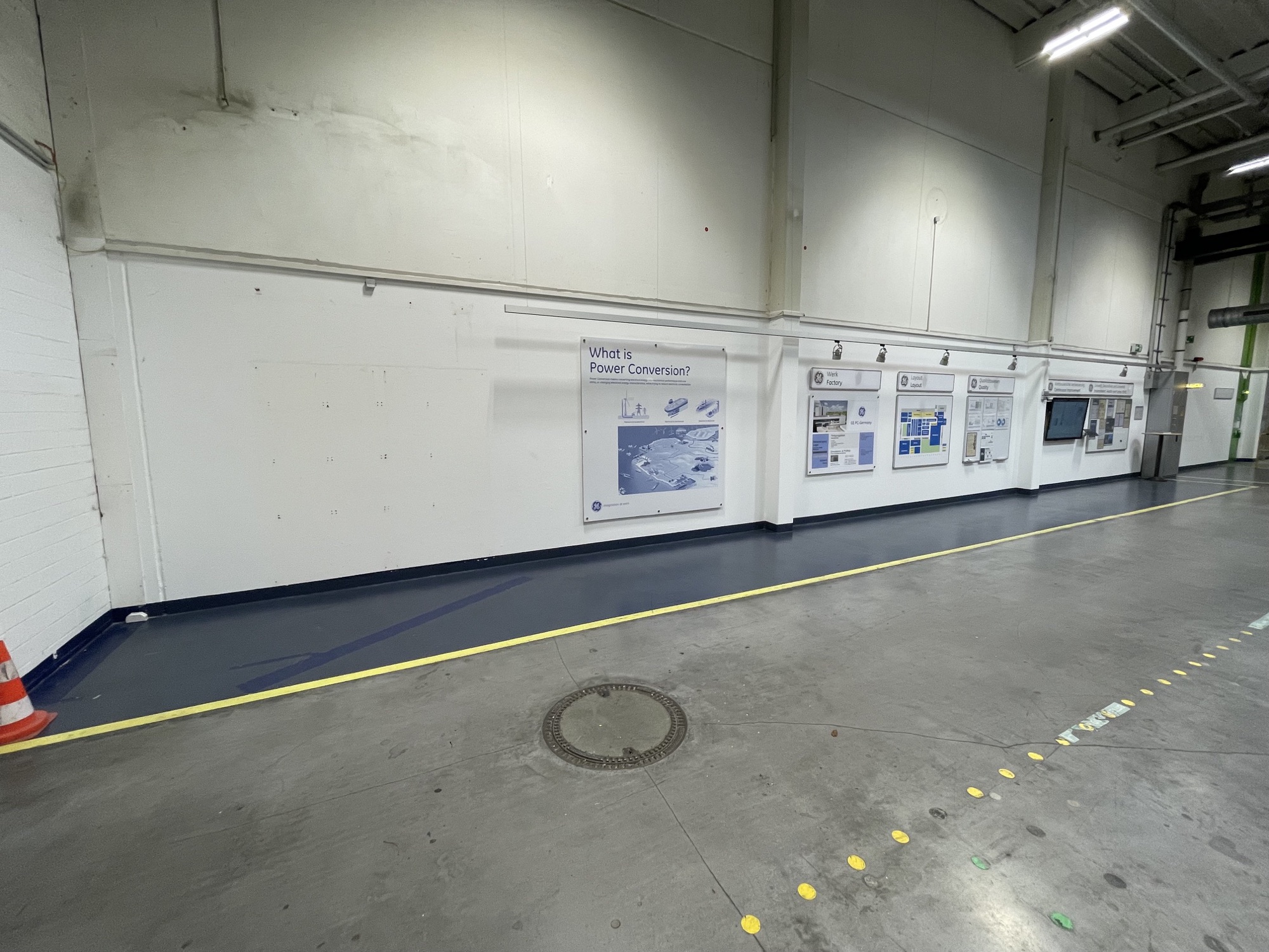 Weiße Hallenwand mit Info-Tafeln vor dem Umbau in der GE-Vernova-Produktionshalle