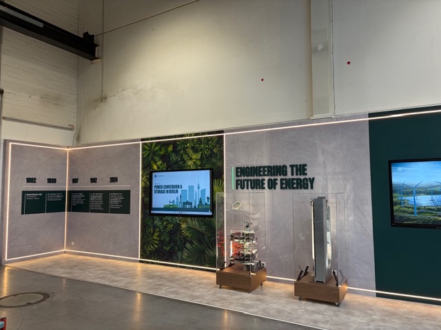 Showwand in der GE-Vernova-Produktionshalle mit Zeitstrahl, 3D-Claim, Vitrinen und Touchmonitor