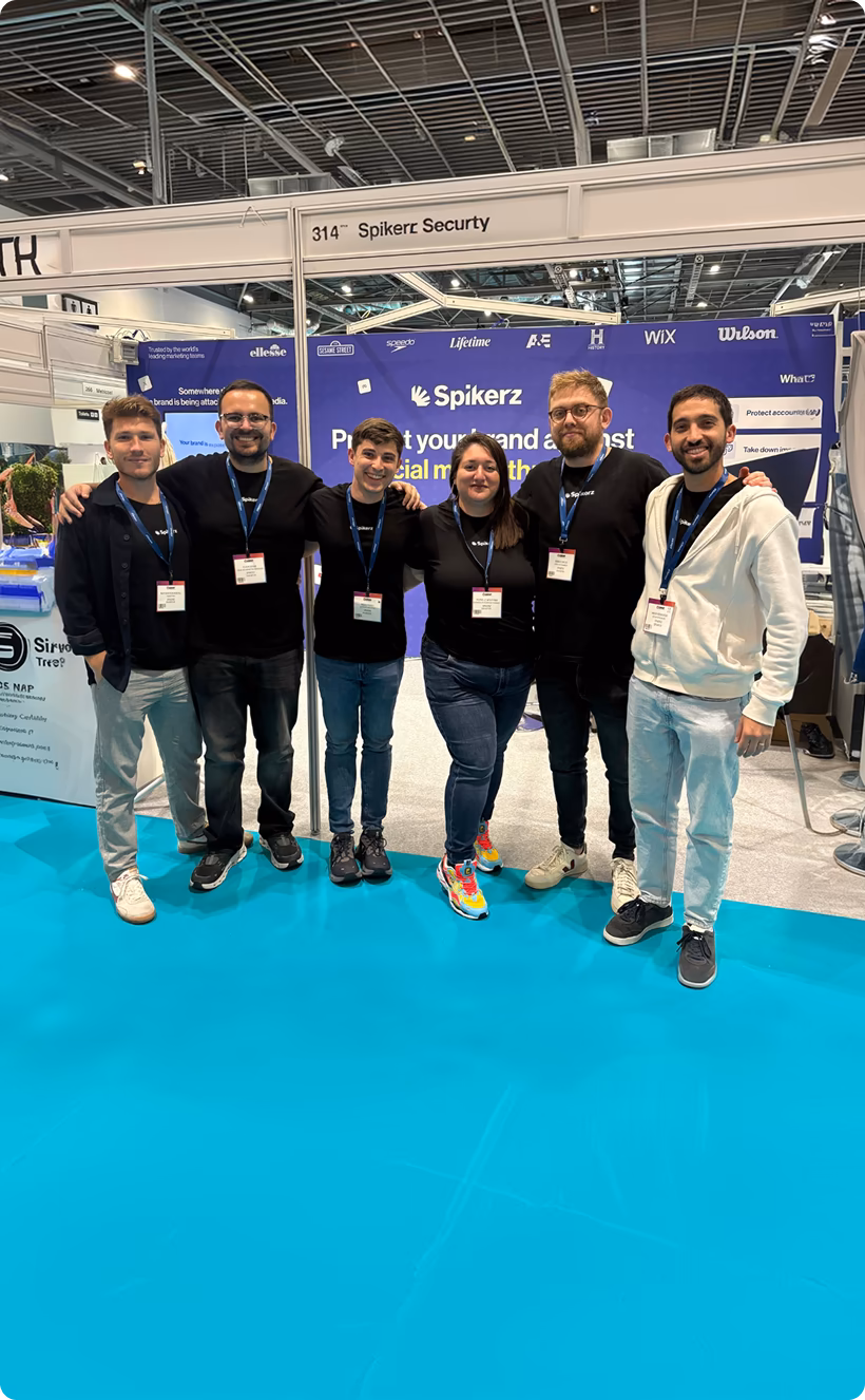 Six people standing side by side at a Spikerz Security booth with a blue carpet and backdrop.