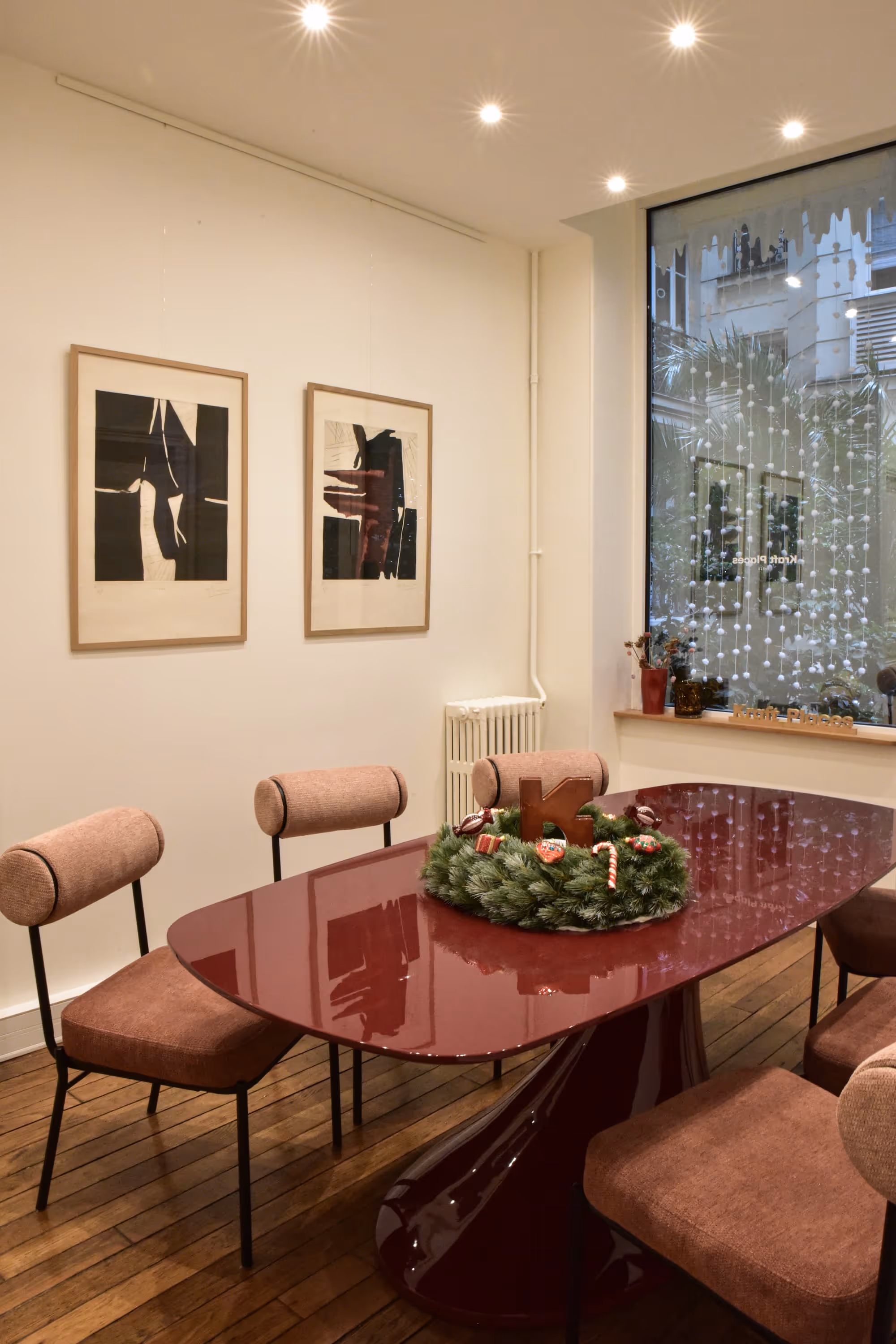 Salle à manger moderne avec table rouge brillante, quatre chaises roses et une décoration de couronne de Noël au centre.