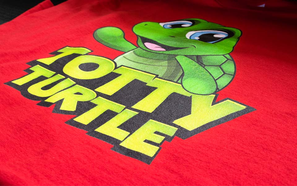 Grüne Schildkröte mit Aufschrift "Totty Turtle" auf rotem Shirt