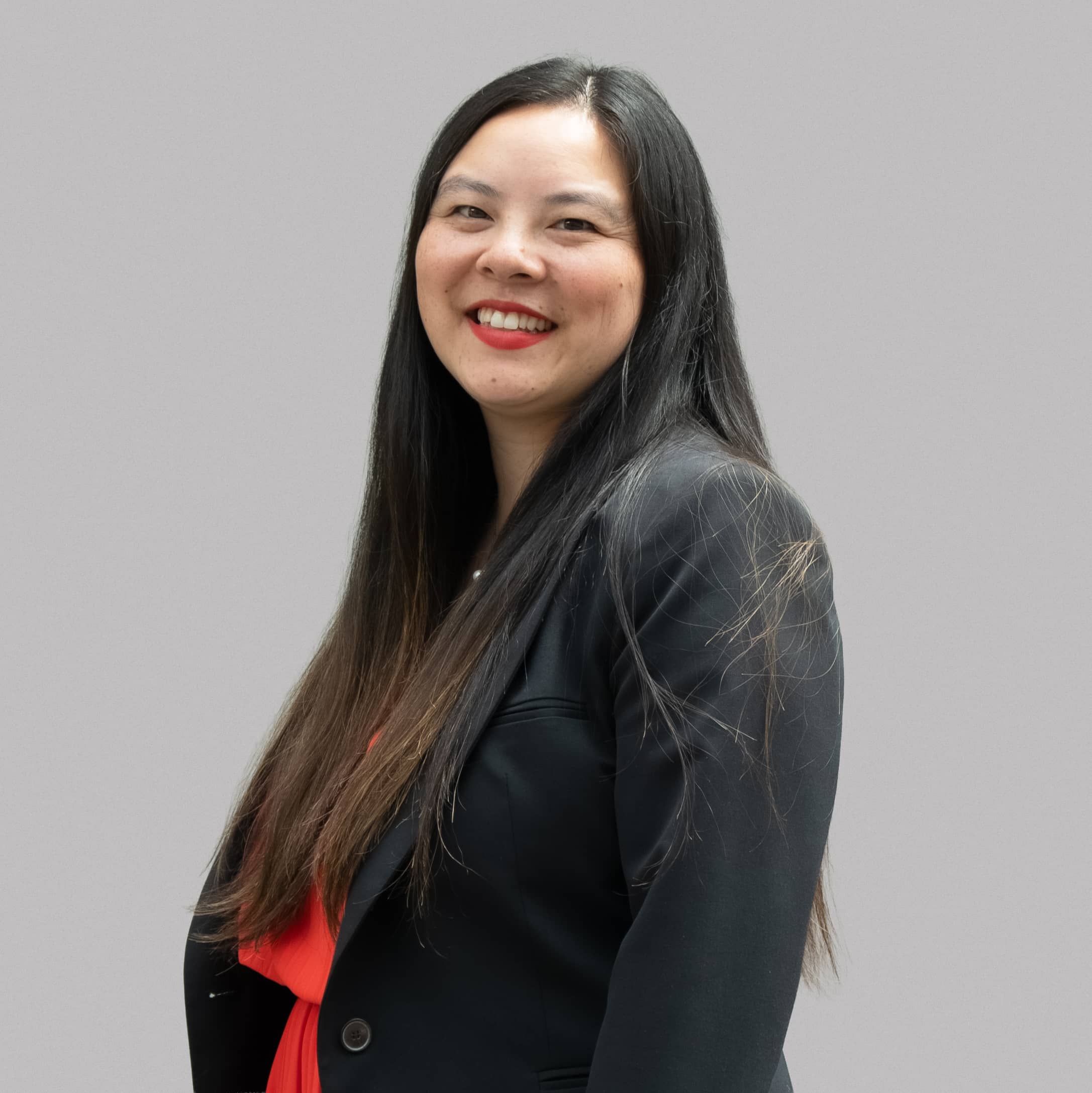 Portrait de Lio, conseillère en communication citoyenne à l'agence Well. Elle est vêtue d'une robe rouge et d'un veston, et a les cheveux noirs.