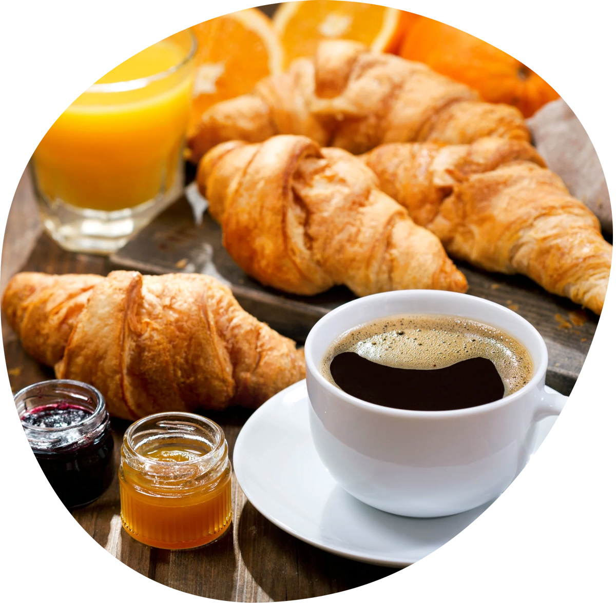 Breakfast with croissants, black coffee in white cup, orange juice, and jam jars on wooden table.