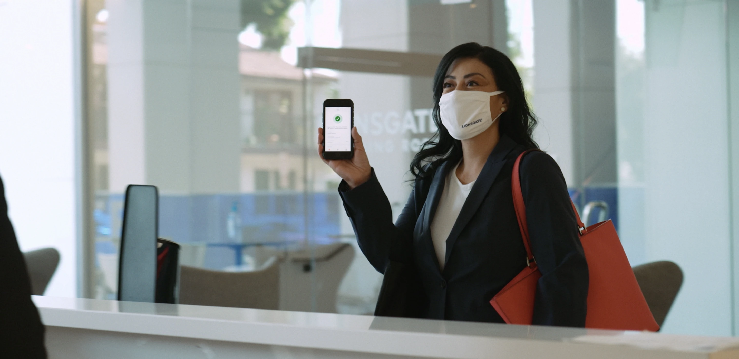 A person wearing a face mask and holding up their phone to check in to a workplace