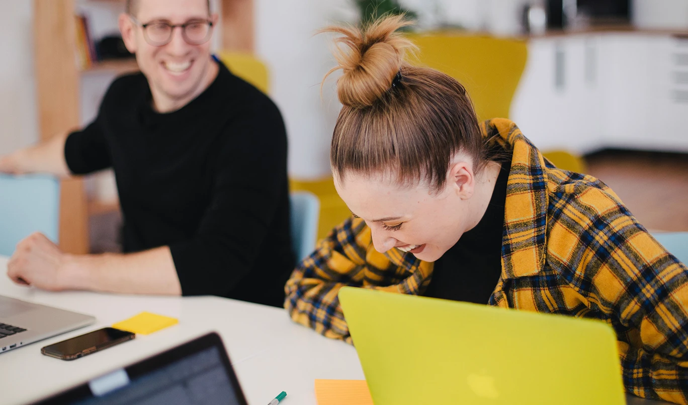 Two people sitting at a conference table and laughing