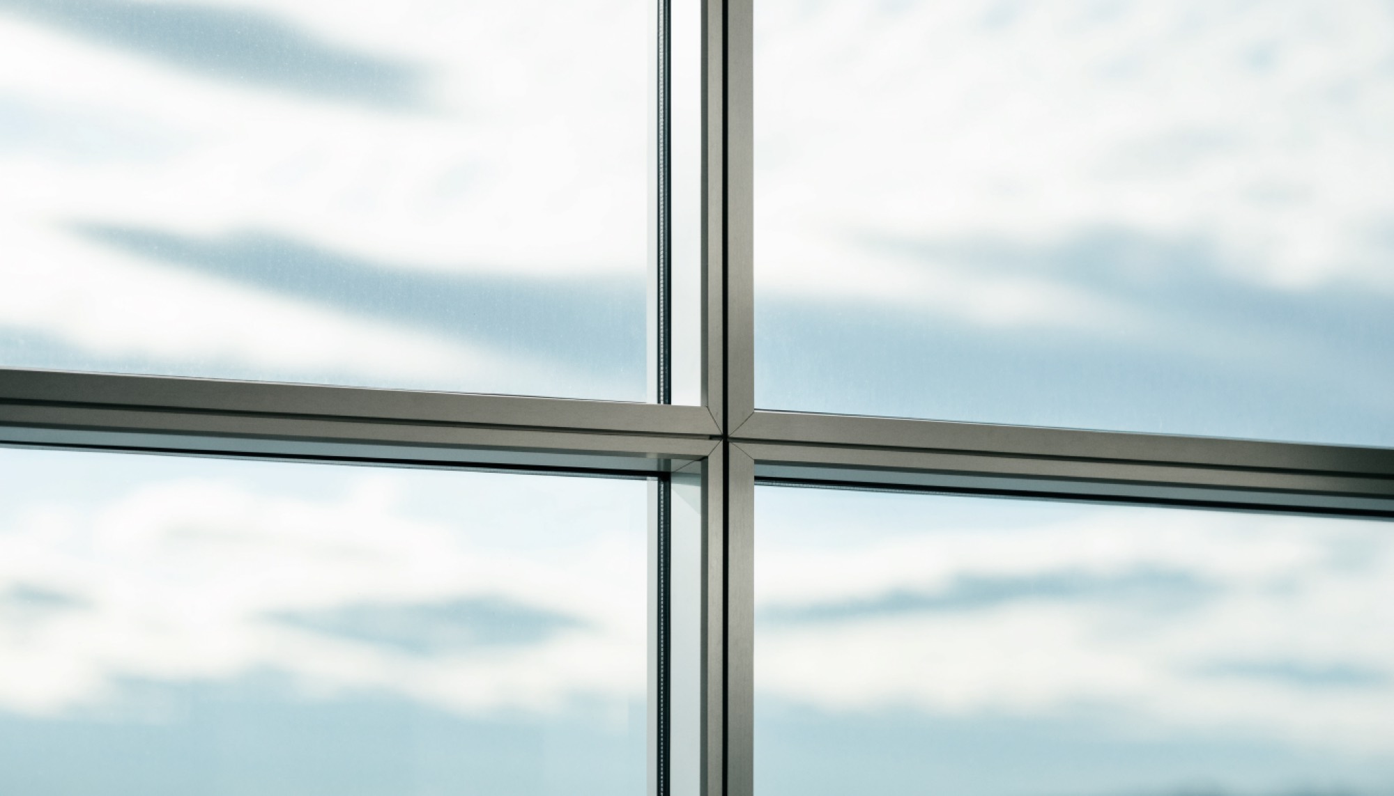 Marco de un ventanal de oficina de piso a techo con cielo azul y nubes altas al fondo