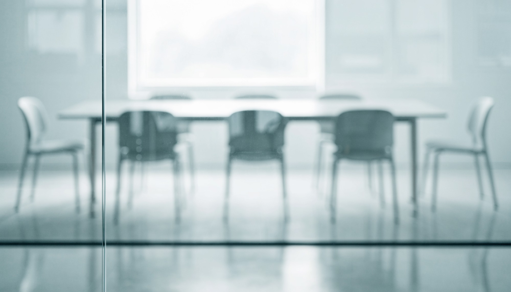 Sala de reuniones vacía con mesa blanca y sillas, vista a través de un tabique de vidrio