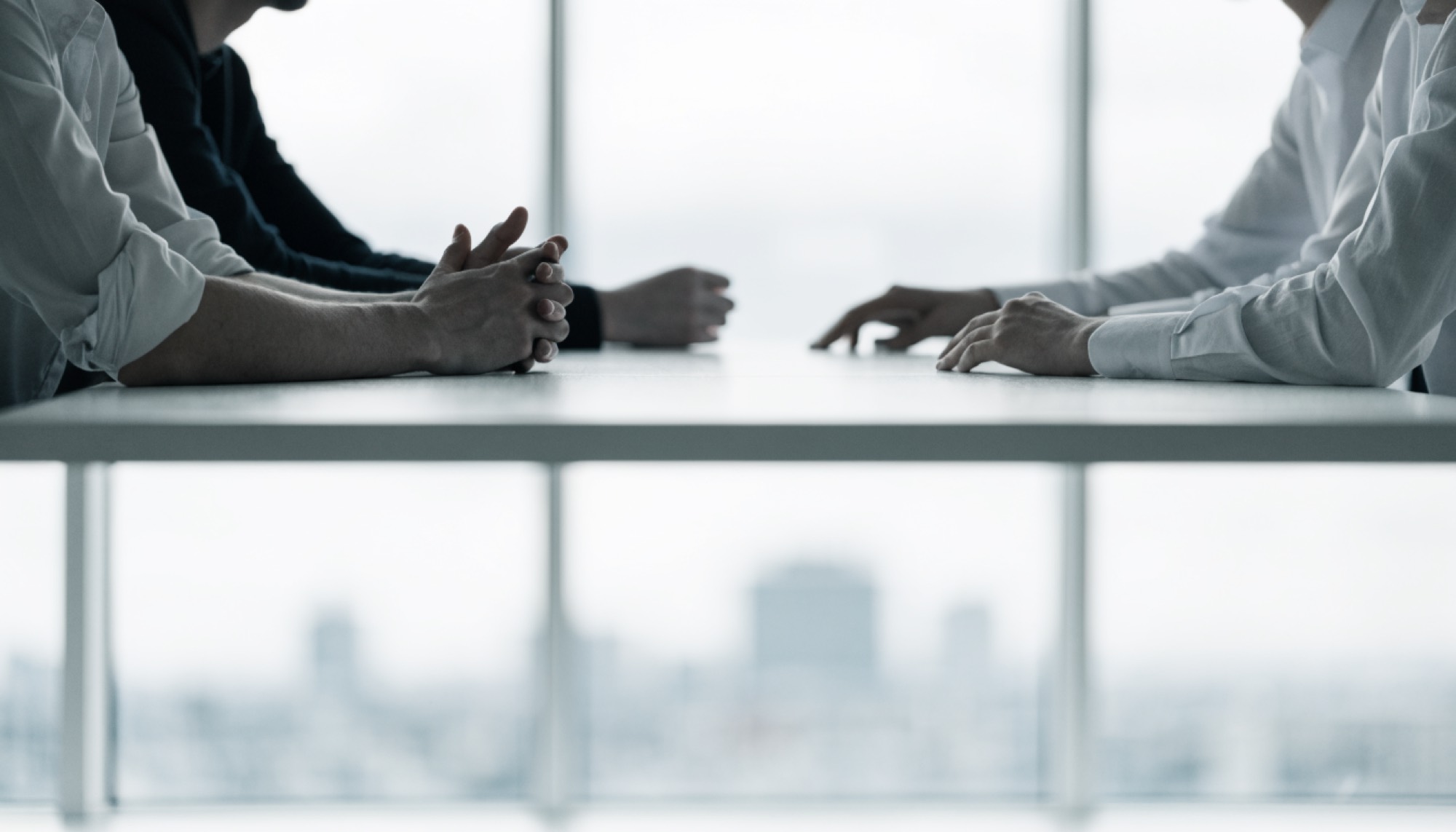 Dos profesionales conversando en una mesa de reuniones blanca con vista a la ciudad a través del ventanal