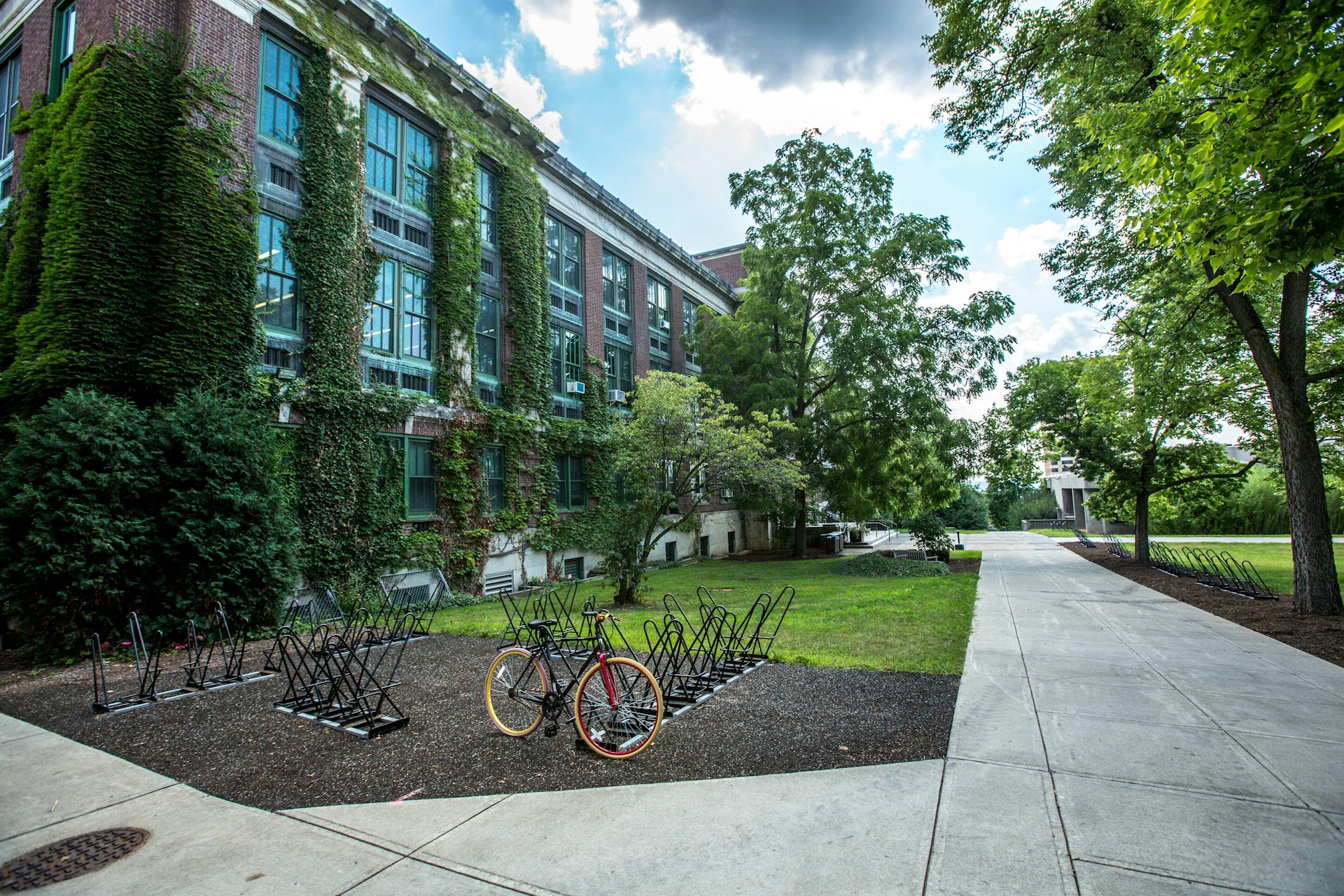 College campus shows neat lawns and walkways near a bicycle rack with one bike. 