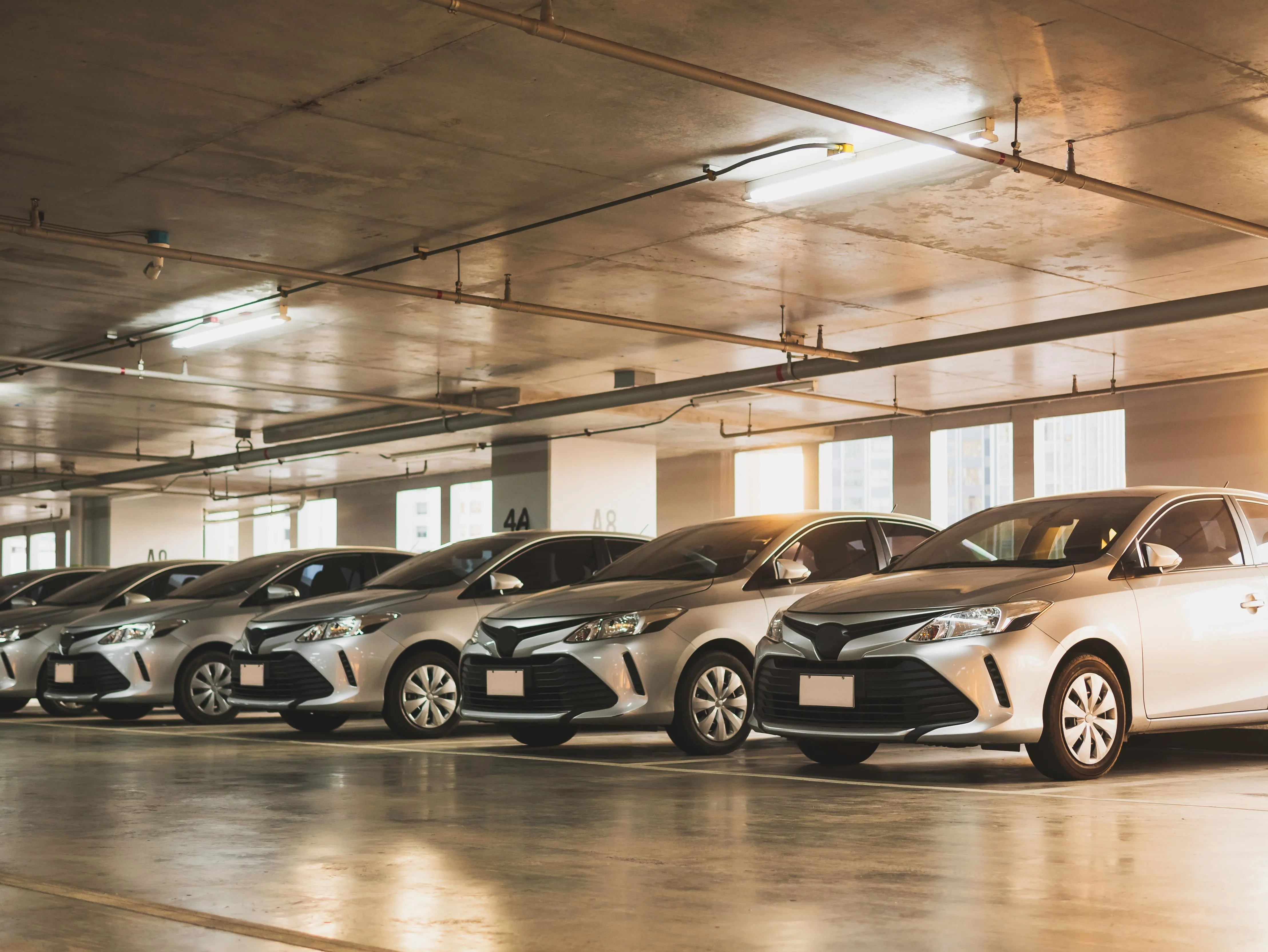 A row of silver sedans parked neatly in an indoor parking garage under fluorescent lights.
