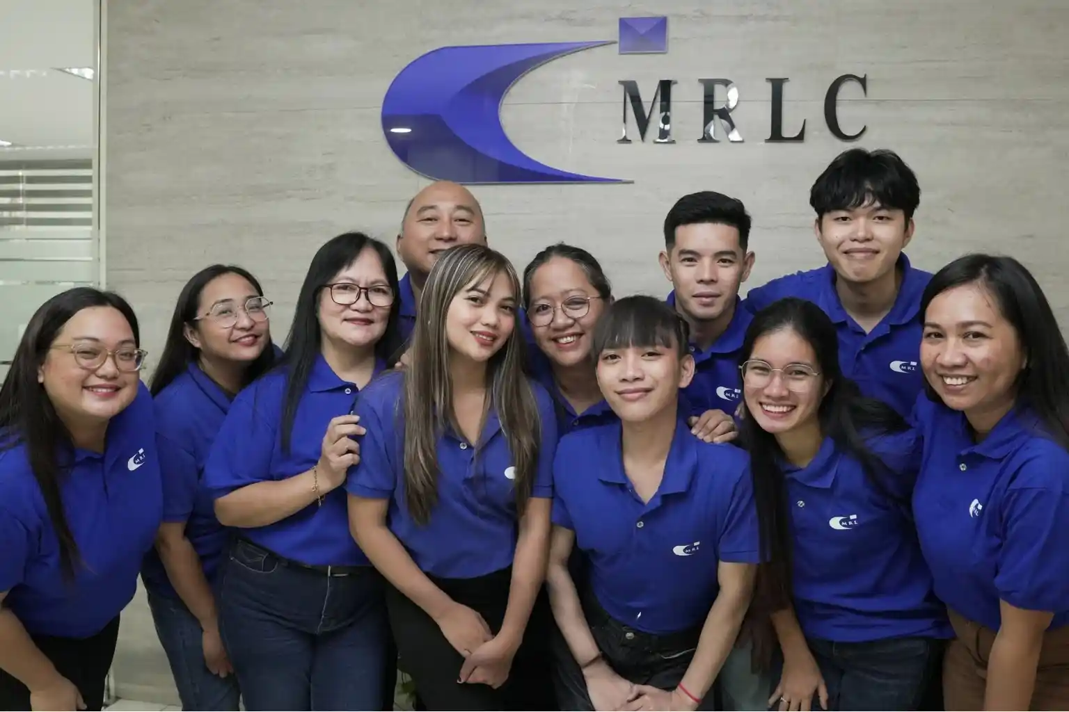 A group of eleven people wearing blue polo shirts posing and smiling in front of an MRLC logo wall.