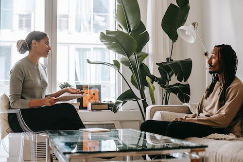Free Side view of professional female African American therapist sitting in front of black male patient during psychotherapy session in office Stock Photo