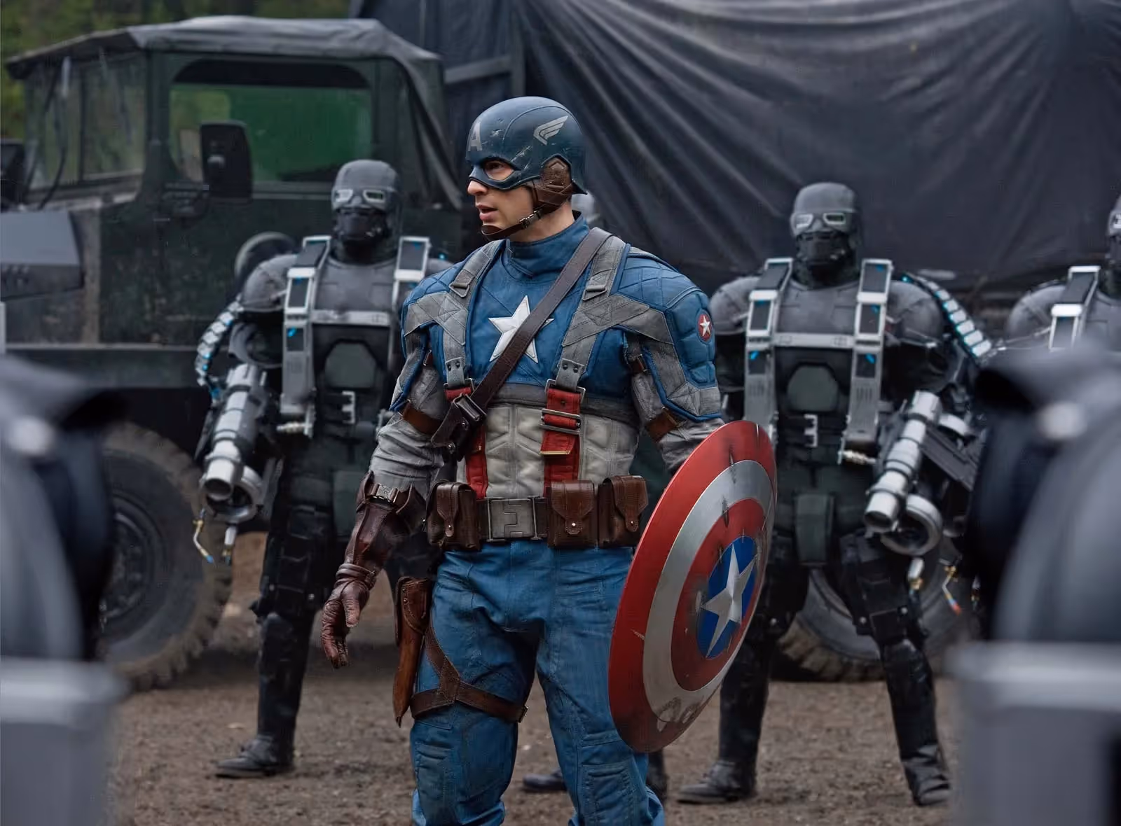 Chris Evans with Captain's America shield, other characters and a military truck in the back