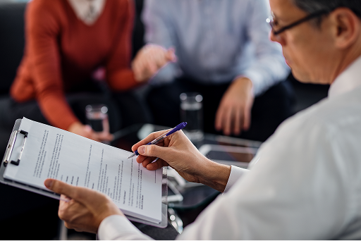 The image shows a professional reviewing and completing a document with a purple pen while others sit at a conference table with water glasses.