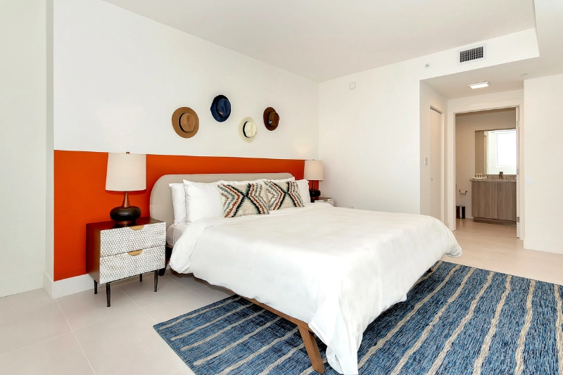 bedroom with orange headboard wall white bedding and blue striped rug at grove 27 by roami