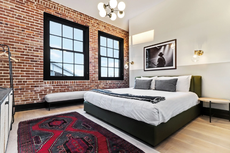 bedroom with exposed brick wall large windows and red rug at the lola by roami