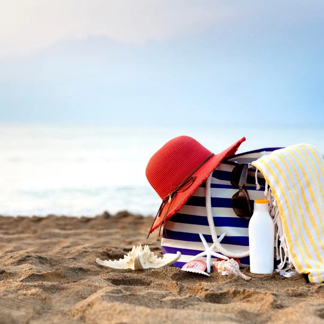 red sun hat striped beach bag and sunscreen on the sand by the sea
