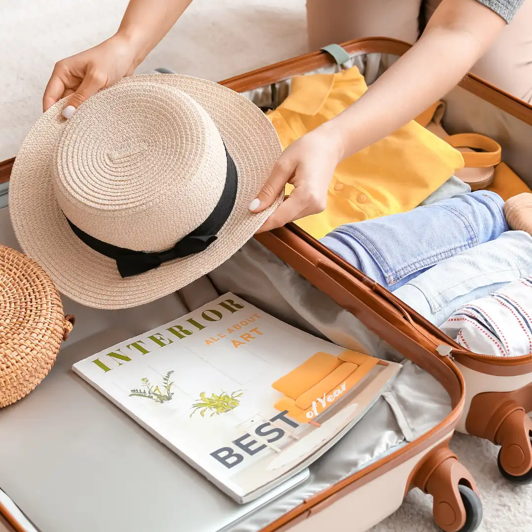 person packing a suitcase with a sun hat clothes and travel guide