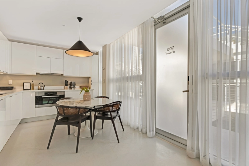 white kitchen and round dining table with pendant light and sheer curtains