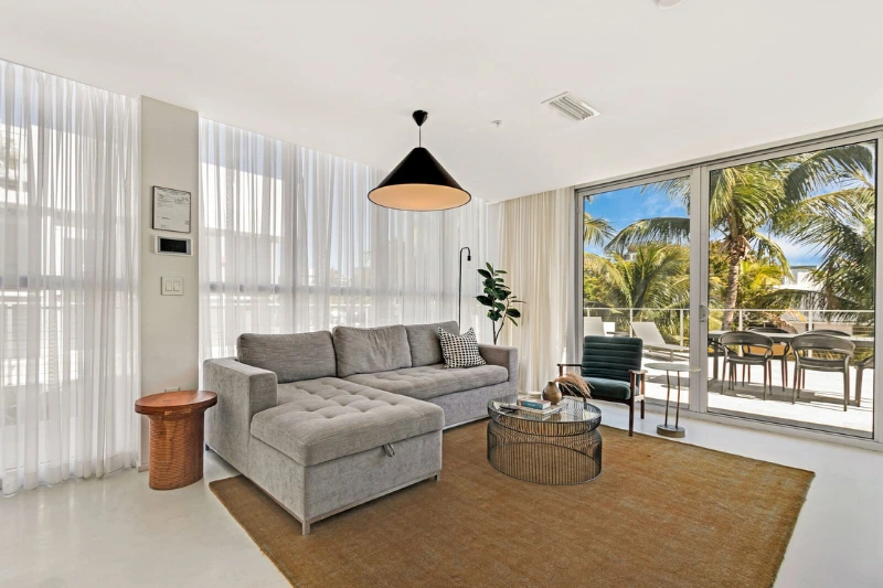 living room with grey sectional sofa and sliding doors to a terrace with palm trees