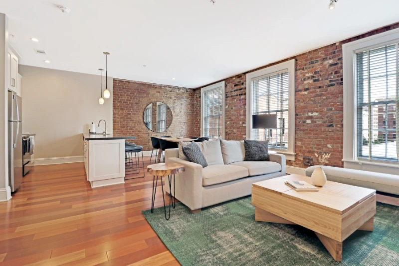 open living area with exposed brick walls hardwood floors and green rug in a roami apartment