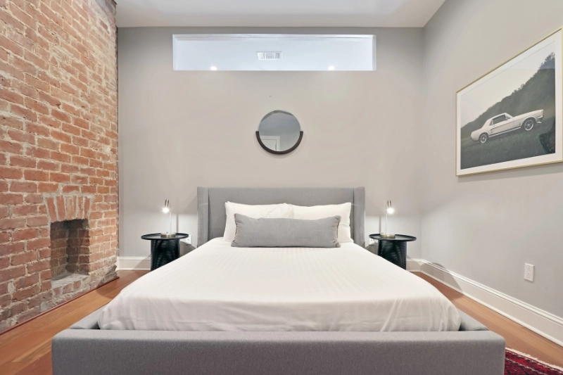 minimal bedroom with grey upholstered bed and brick fireplace in a roami apartment