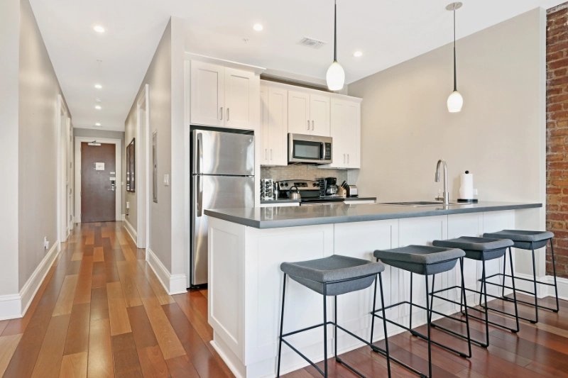 white kitchen with breakfast bar stools and hardwood floors in a roami apartment