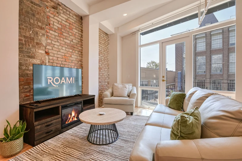 sunlit living room with brick wall fireplace and large windows in a roami apartment