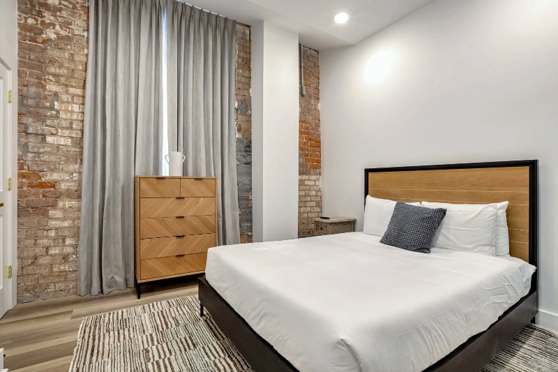 bedroom with exposed brick wall wooden dresser and queen bed in a roami apartment